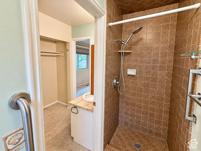 Walk-in shower featuring textured ceramic tile surround, integrated shower shelving, and an adjustable handheld showerhead