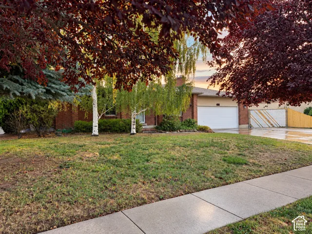 Brick exterior featuring a two-car garage, concrete driveway, and mature landscaping