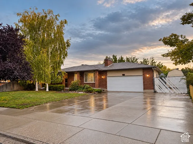 Single-story residence featuring brick exterior cladding, a multi-car garage, expansive concrete driveway, and mature landscaping