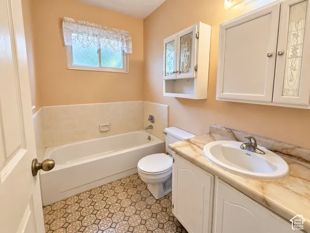Bathroom featuring a white bathtub with tile surround, vanity with a stone-finish countertop and integrated sink, and white wall-mounted cabinetry with decorative glass inserts