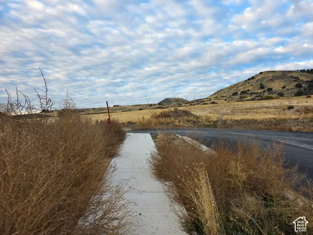 Concrete sidewalk surfacing, asphalt roadway, and surrounding rolling terrain