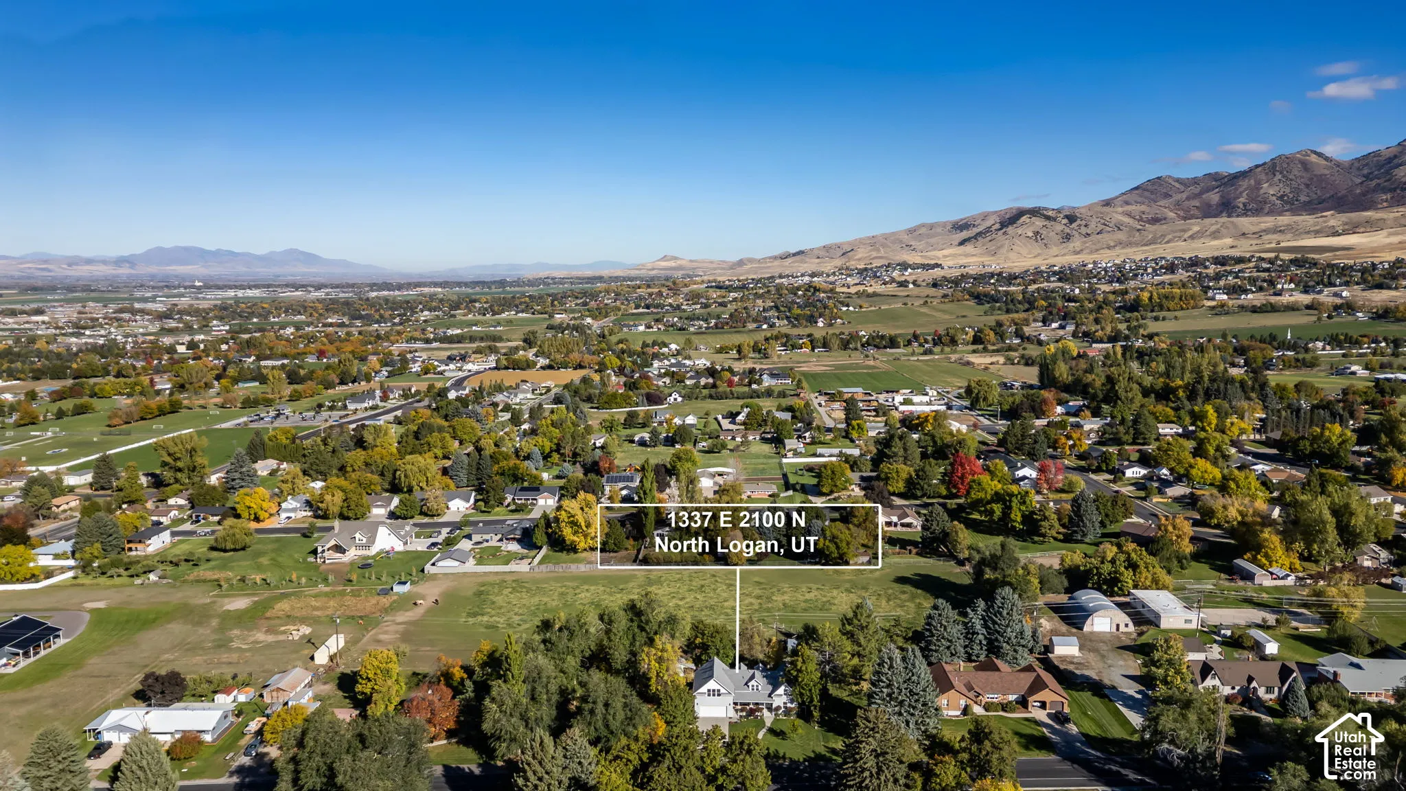 Aerial perspective of a multi-level residence situated on a landscaped lot featuring mature trees and mountain backdrops