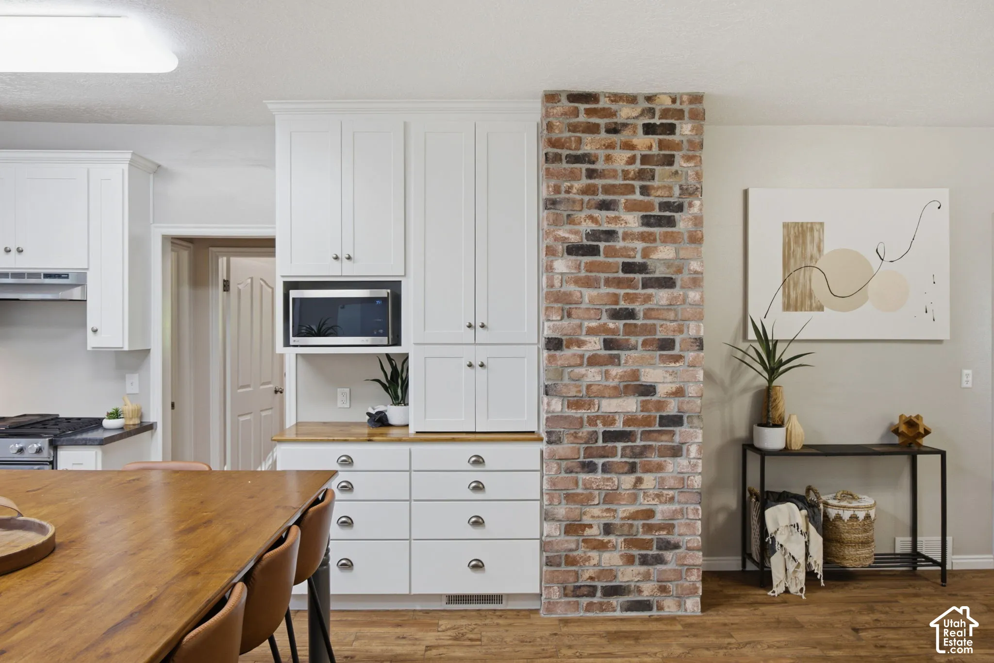 Kitchen featuring white shaker-style cabinetry, wood-finish countertops, multi-tonal brick accent wall, and wood-finish flooring