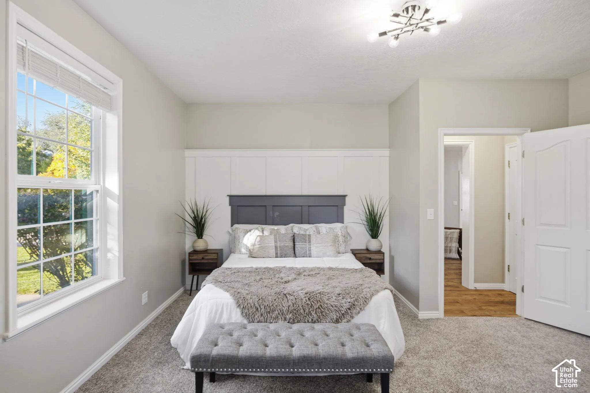 Interior space featuring wall-to-wall carpeting, white wainscoting with a dark-tone built-in headboard accent, multi-pane window, and geometric flush-mount lighting