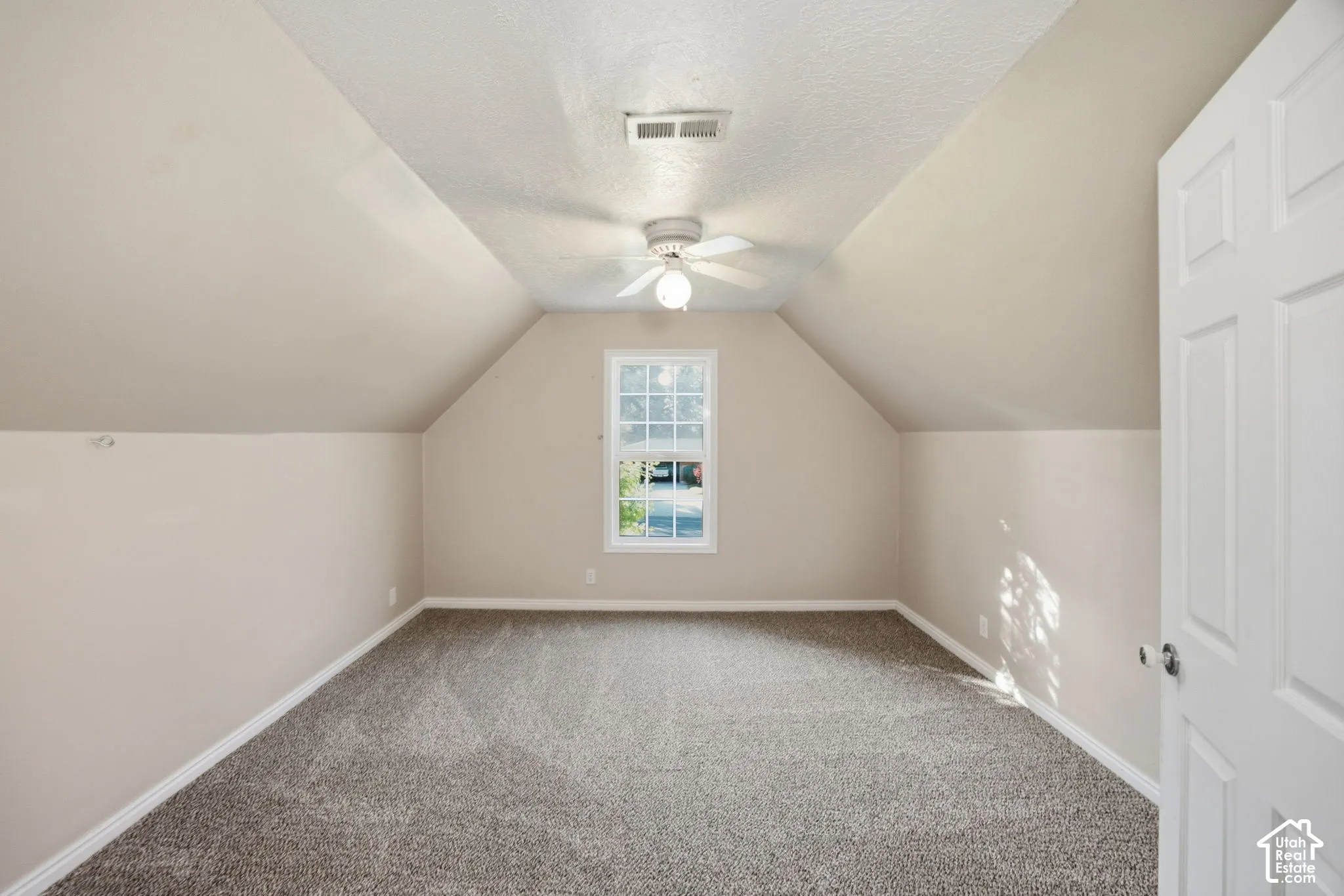 Interior space featuring vaulted ceilings, neutral-toned wall paint, wall-to-wall carpeting, a center-mounted ceiling fan with integrated lighting, and a single-pane window