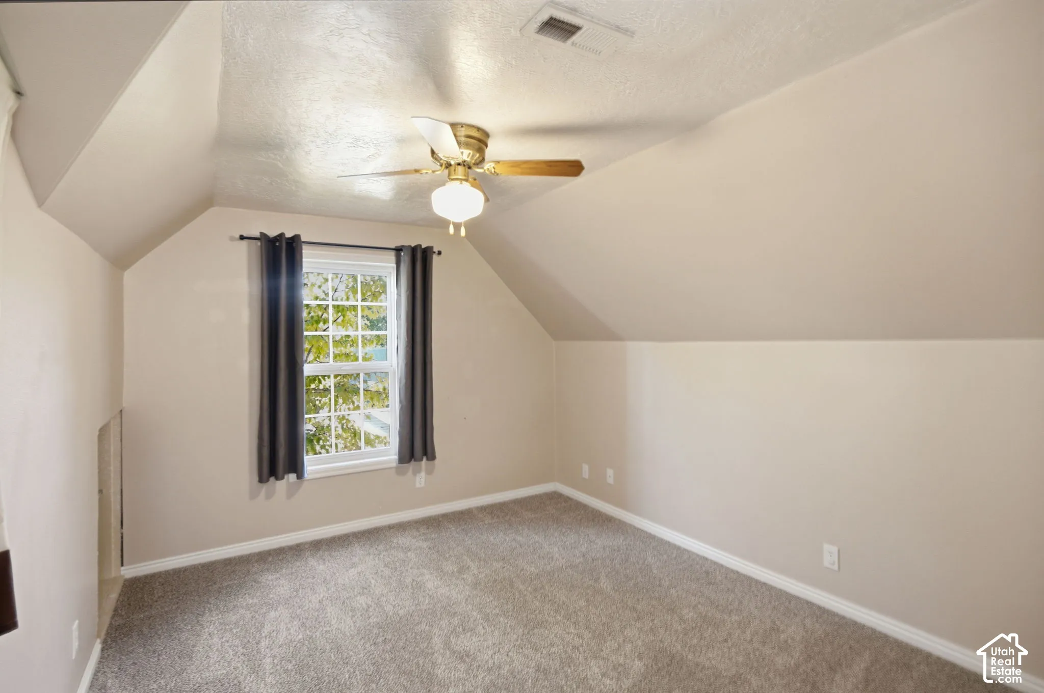 Room featuring vaulted ceilings, neutral-toned walls, wall-to-wall carpeting, and a central ceiling fan with an integrated light fixture