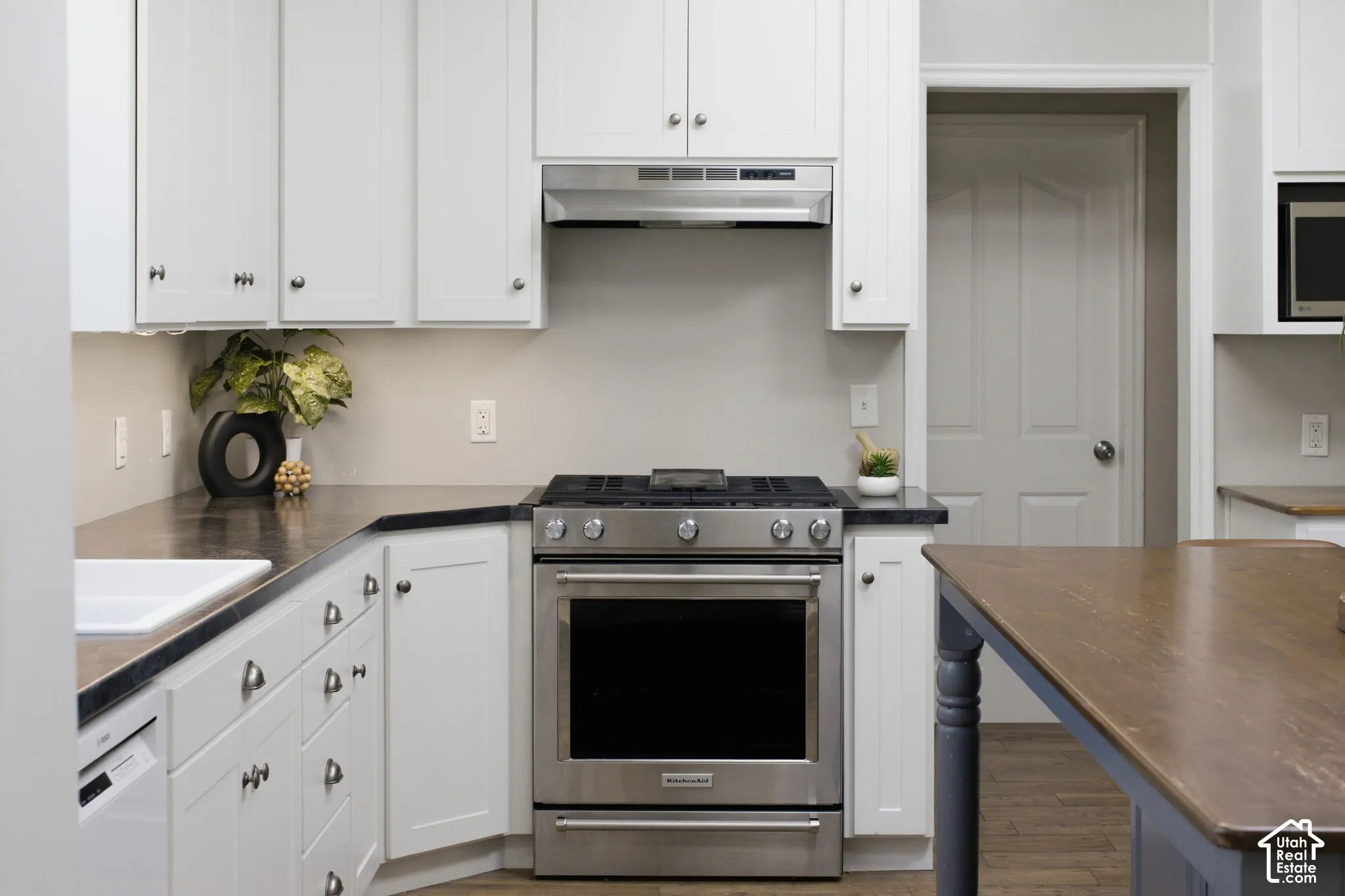 Kitchen featuring white shaker-style cabinetry, dark stone countertops, stainless steel gas range, integrated vent hood, and wood-finish flooring