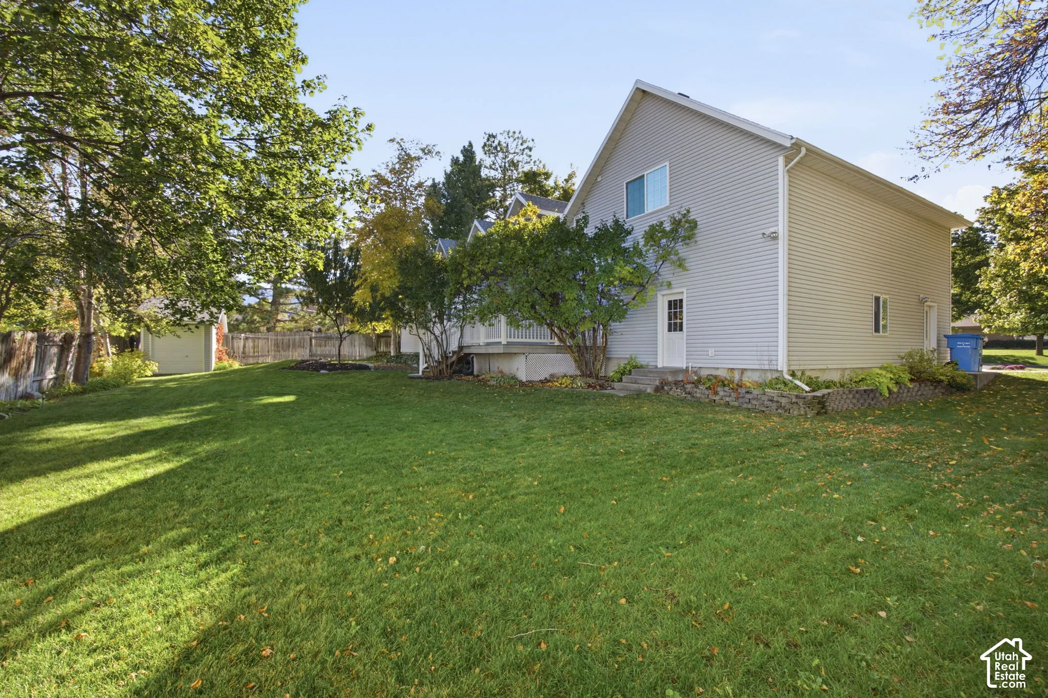 Exterior featuring light-colored horizontal siding, a fenced yard, mature trees, and a detached structure