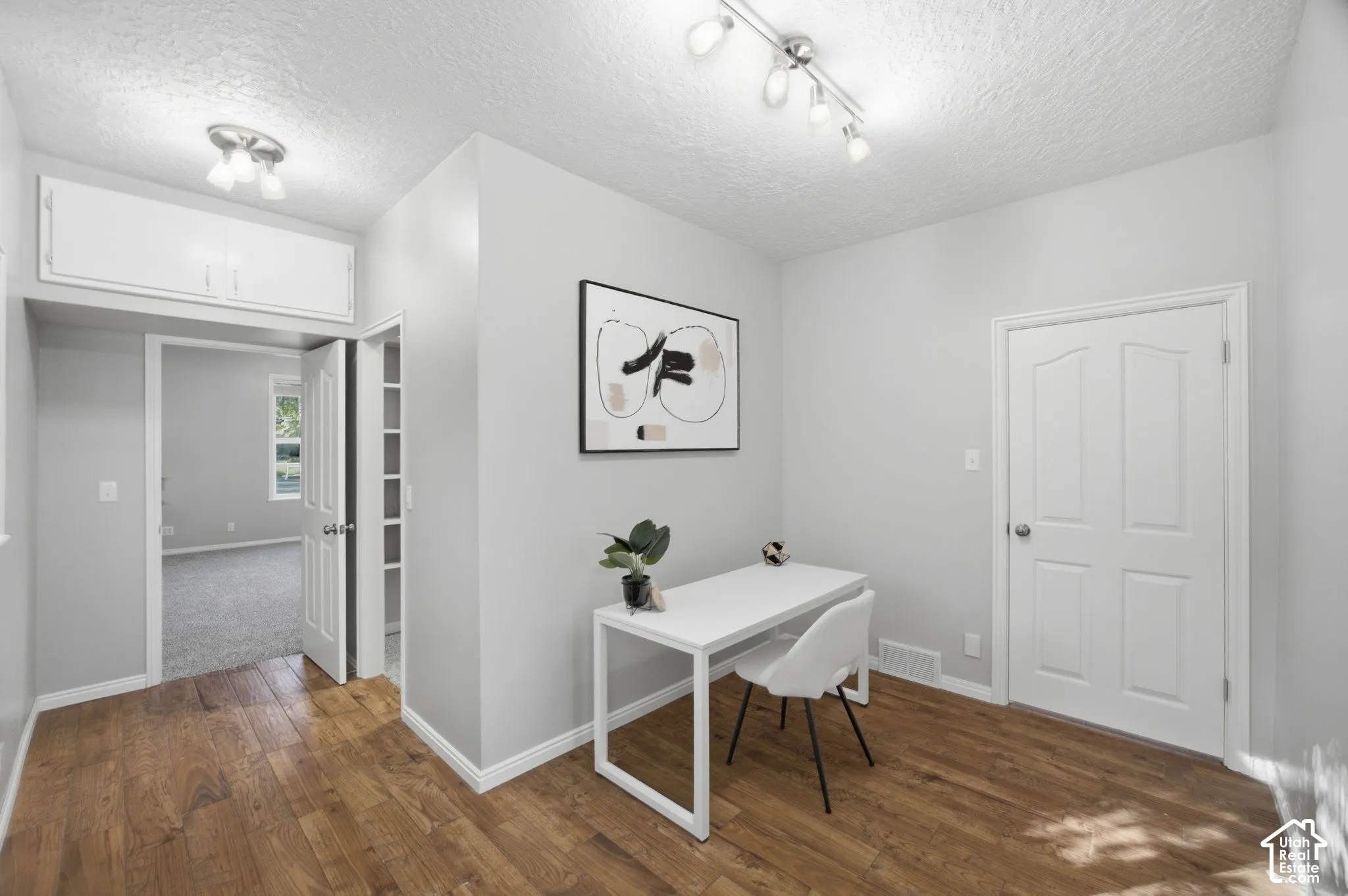 Room featuring wood-finish flooring, built-in overhead storage cabinetry, adjustable multi-bulb track lighting, and a neutral color palette