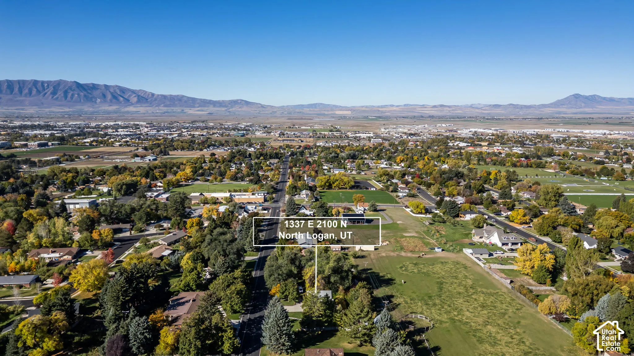 Aerial perspective of the property in North Logan, Utah, featuring expansive grounds, mature trees, and prominent mountain range scenery