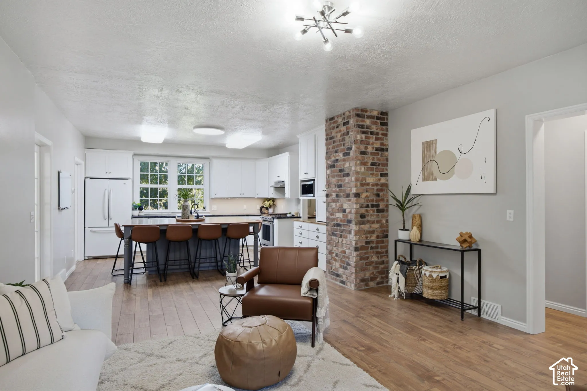 Kitchen featuring white cabinetry, wood-finish flooring, a central island, and a distinctive exposed brick column