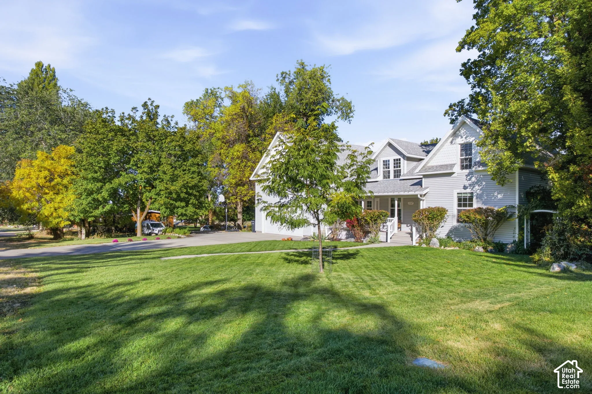 Two-story residence featuring grey lap siding, an expansive front lawn, mature trees, a multi-gabled roofline, and an asphalt driveway