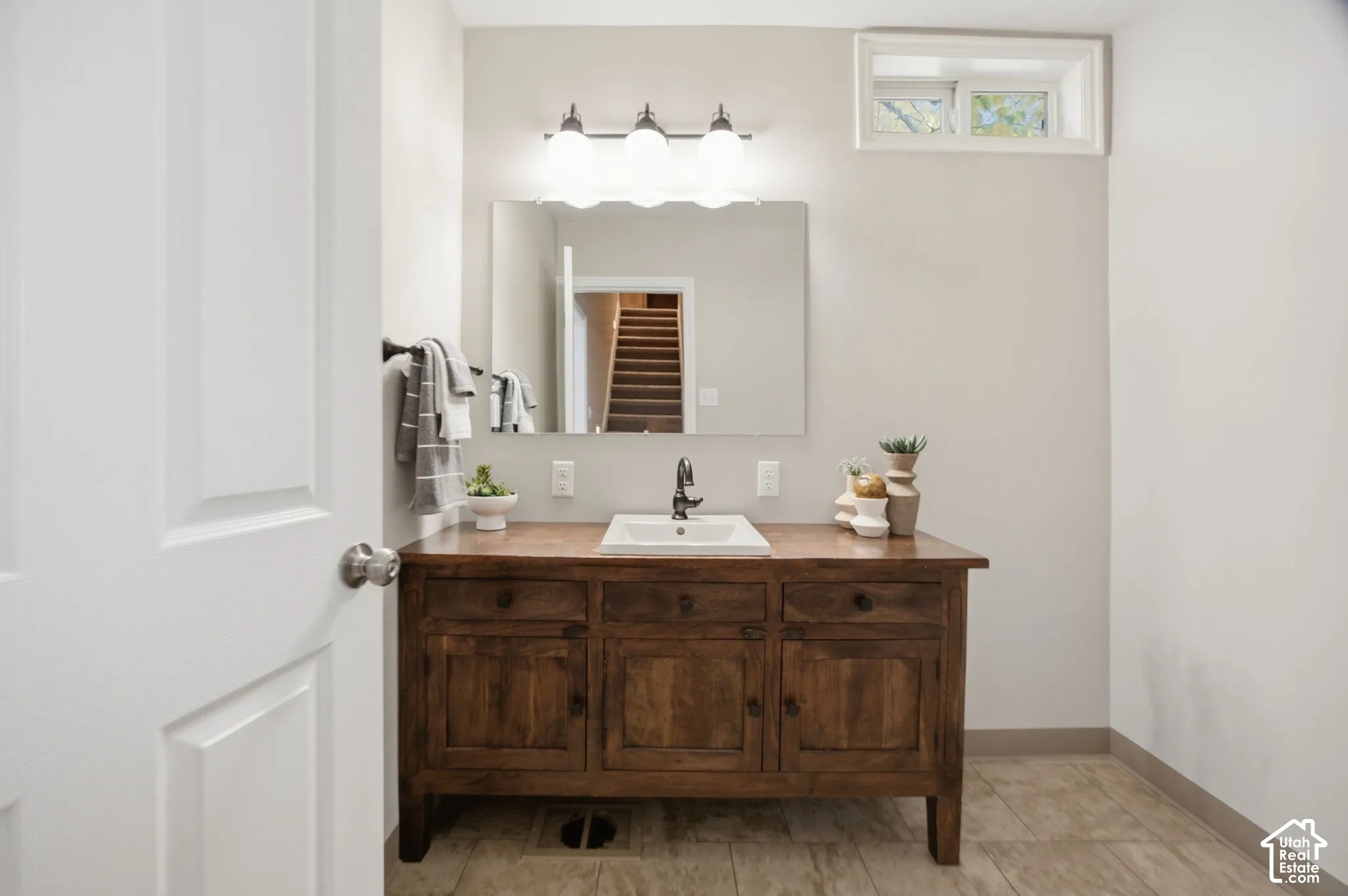 Bathroom vanity featuring a stained-wood cabinet base, inset rectangular basin, polished metal faucet, wall-mounted mirror, and triple-light fixture
