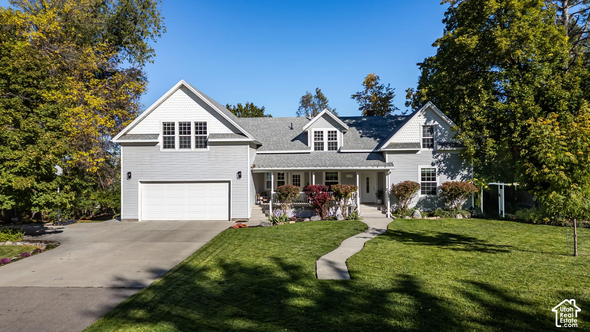 Two-story residence with light gray siding, an expansive attached garage, a covered front porch, a concrete walkway, and a manicured lawn