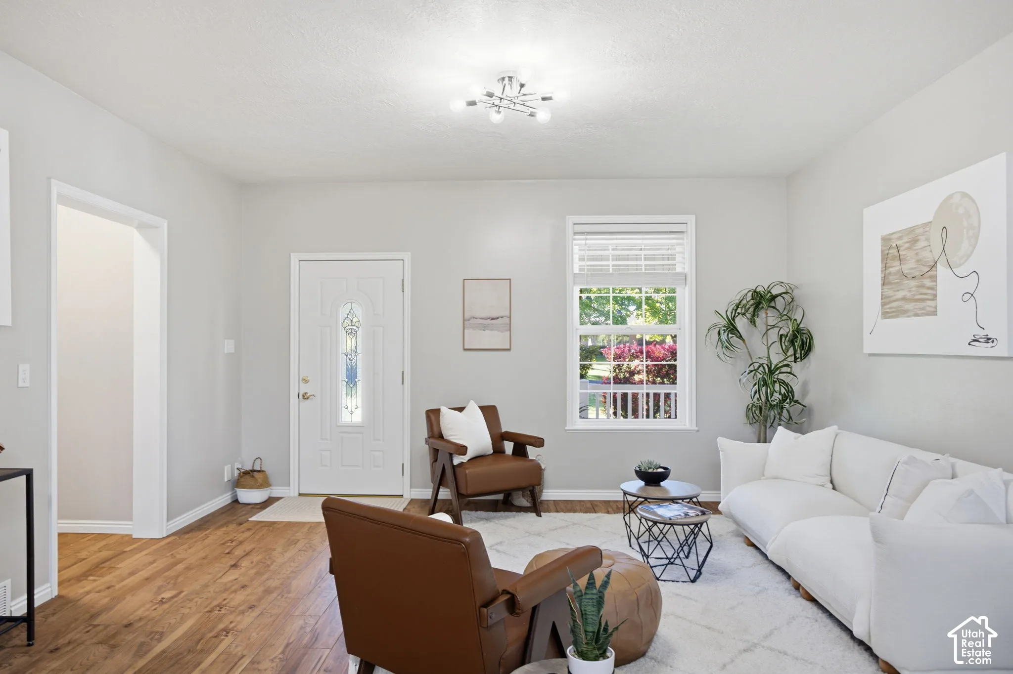 Living area featuring wood-finish flooring, a multi-bulb ceiling fixture, a window with horizontal blinds, and an exterior door with decorative glass inlay