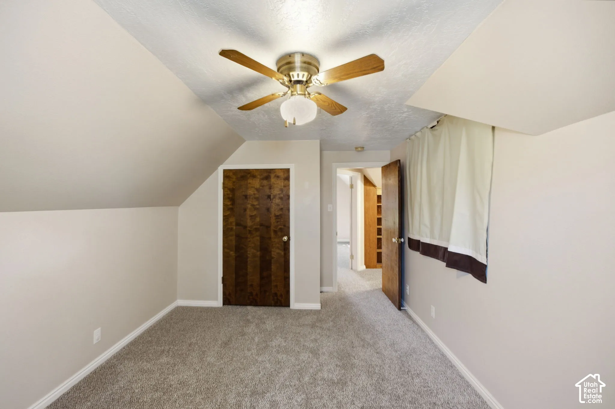 Sloped ceiling room featuring wall-to-wall carpeting, wood-grain interior doors, and a central ceiling fan with integrated light fixture