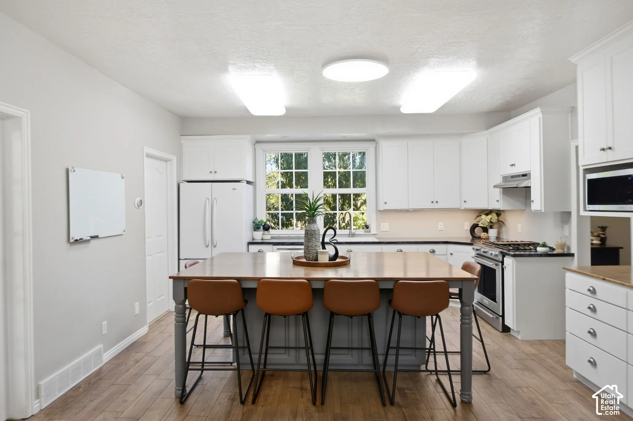 Kitchen featuring white cabinetry, wood-finish flooring, a central island with a wood countertop, stainless steel appliances, and multi-pane windows