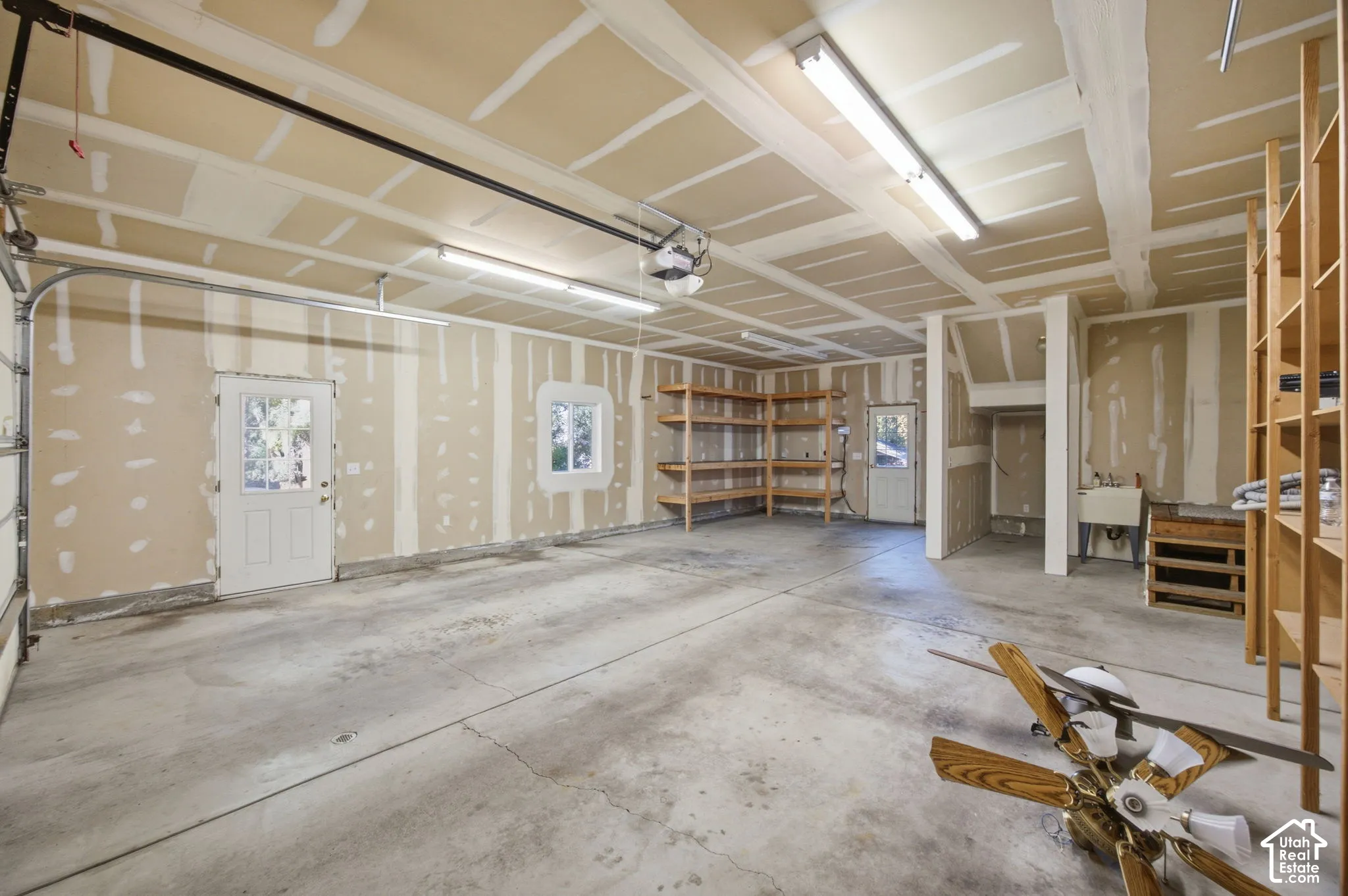 Multi-car garage featuring a concrete floor, built-in wooden shelving, utility sink, and two external access doors