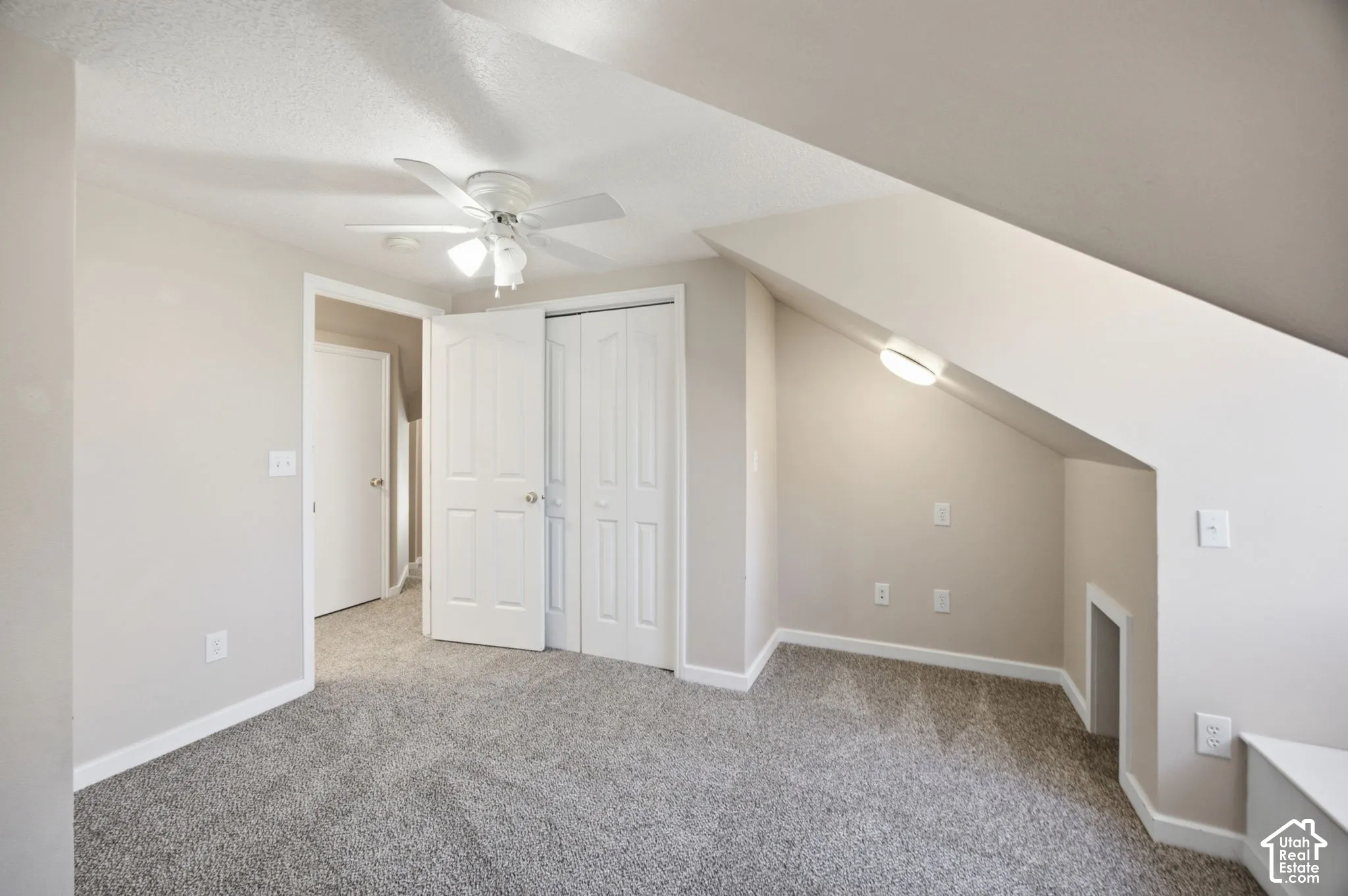 Vaulted ceiling with architectural dormer, neutral carpeting, ceiling fan with integrated lighting, and white six-panel closet doors