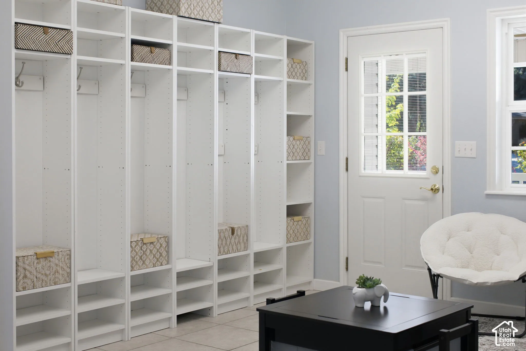 Custom white built-in cabinetry featuring floor-to-ceiling storage units with integrated shelving and wall-mounted hooks, complemented by a white exterior door with multi-pane glass inserts and light-toned tile flooring