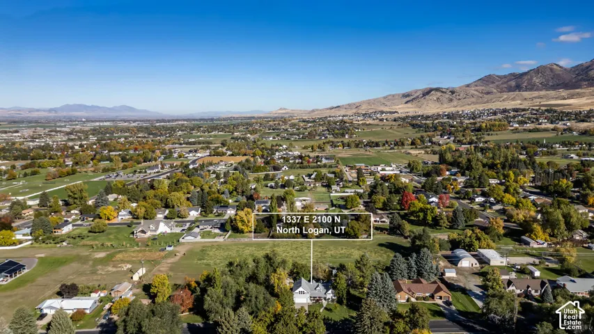 Aerial perspective of a multi-level residence situated on a landscaped lot featuring mature trees and mountain backdrops