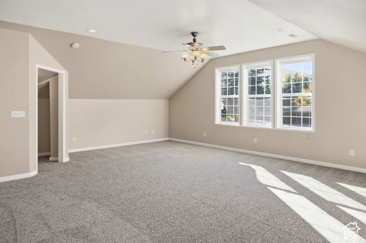 Spacious room featuring a vaulted ceiling, neutral wall tones, wall-to-wall carpeting, three-pane window configuration, and a central ceiling fan with multi-light fixture