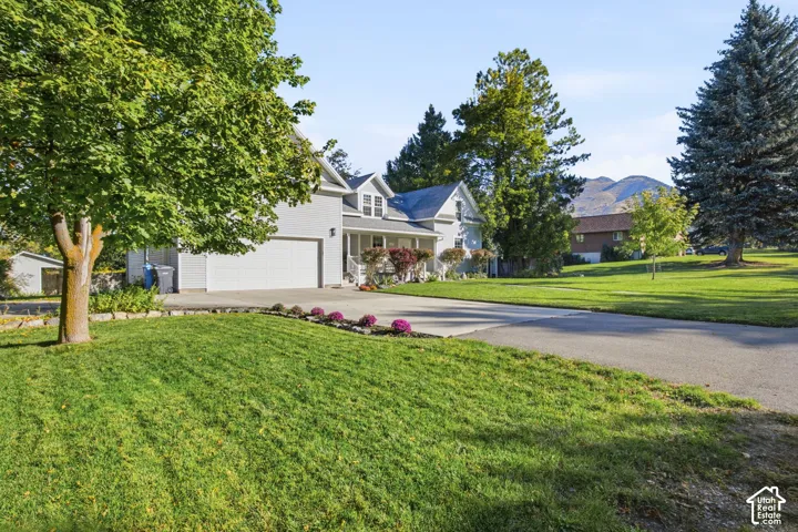 Two-story residence featuring light gray siding, an attached two-car garage, an expansive lawn, mature shade trees, and a mountain backdrop