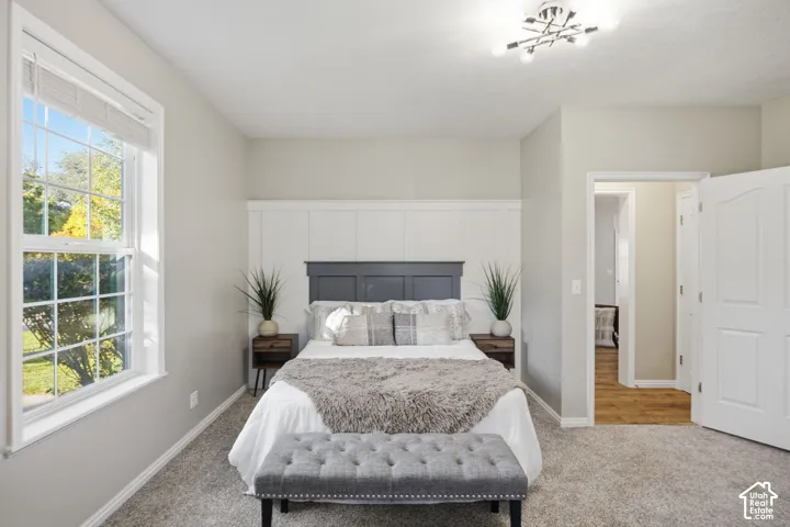 Interior space featuring wall-to-wall carpeting, white wainscoting with a dark-tone built-in headboard accent, multi-pane window, and geometric flush-mount lighting