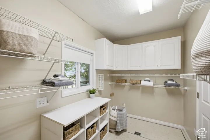 Laundry space featuring white wall-mounted cabinetry, integrated wire shelving, a built-in multi-compartment storage console, and a window for natural light