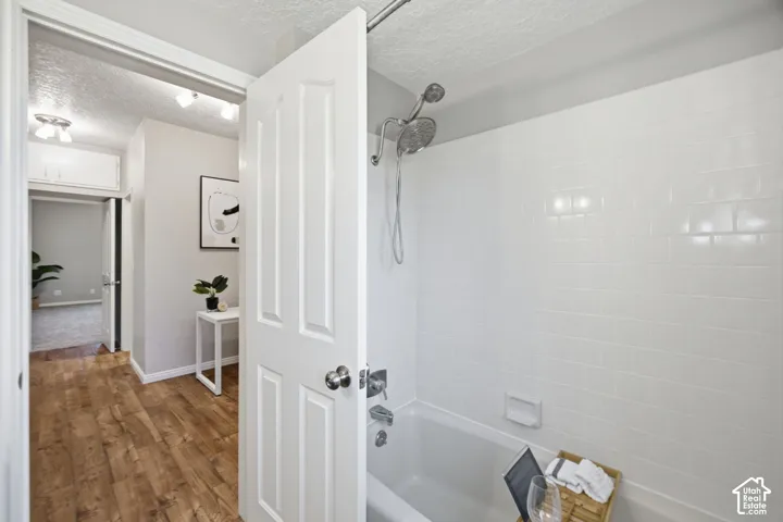 Bathtub with white subway tile surround, chrome shower hardware, and wood-finish flooring