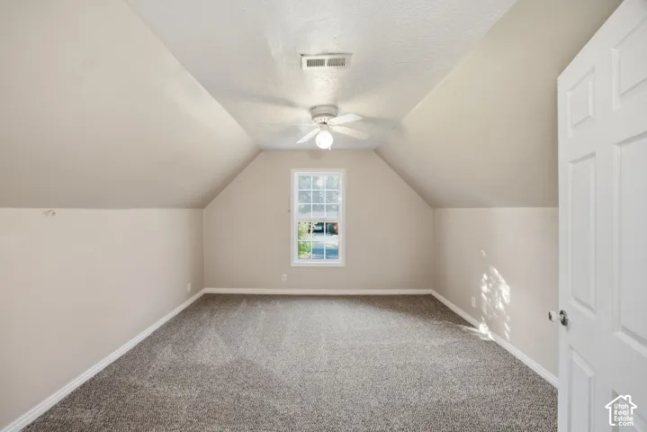 Interior space featuring vaulted ceilings, neutral-toned wall paint, wall-to-wall carpeting, a center-mounted ceiling fan with integrated lighting, and a single-pane window
