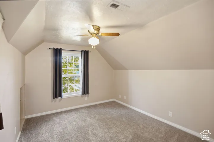 Room featuring vaulted ceilings, neutral-toned walls, wall-to-wall carpeting, and a central ceiling fan with an integrated light fixture
