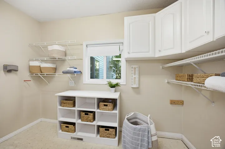 White shaker-style wall cabinets, open wire shelving, built-in cubby storage unit, and vinyl flooring