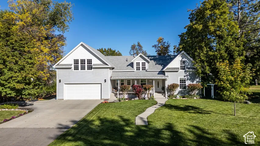 Two-story residence featuring light gray horizontal siding, a covered front porch, an attached two-car garage, multiple gables, and a concrete driveway