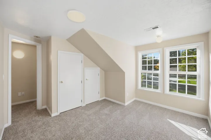Neutral-toned interior room featuring wall-to-wall carpeting, dual multi-pane windows, and built-in under-eave storage cabinetry