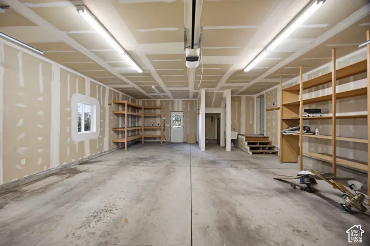 Spacious garage featuring concrete flooring, extensive built-in wood shelving, overhead strip lighting, a utility sink, and a secondary exterior door