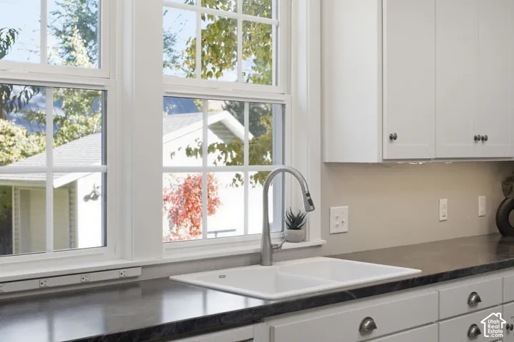 Kitchen featuring white shaker-style cabinetry, dark stone-finish countertops, a dual-basin white sink with a gooseneck faucet, and white mullioned windows