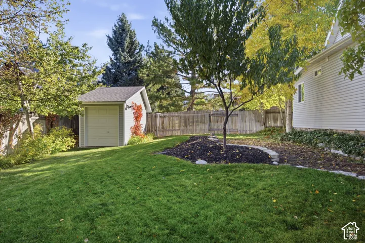 Backyard featuring a detached storage shed, privacy fencing, stone-bordered mulch beds, and mature trees