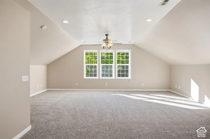 Spacious room featuring vaulted ceilings, neutral wall-to-wall carpeting, recessed lighting, a ceiling fan with integrated light fixture, and a triple-pane window configuration
