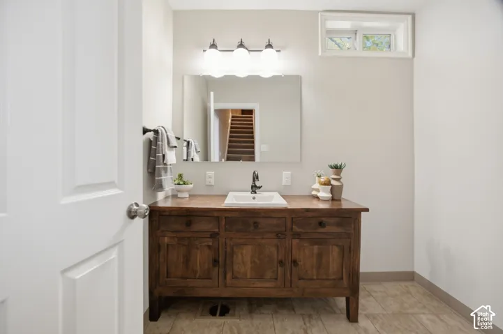 Bathroom vanity featuring a stained-wood cabinet base, inset rectangular basin, polished metal faucet, wall-mounted mirror, and triple-light fixture