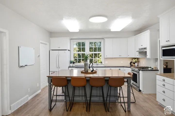 Kitchen featuring white cabinetry, wood-finish flooring, a central island with a wood countertop, stainless steel appliances, and multi-pane windows