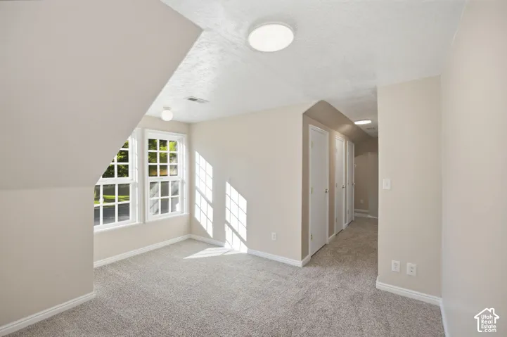 Neutral interior space featuring angled ceilings, dual grid-pattern windows, neutral carpeting, and recessed ceiling lighting