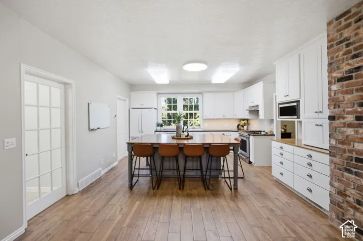 Kitchen featuring white cabinetry, wood-finish flooring, a central island with integrated storage, and a floor-to-ceiling exposed brick accent wall