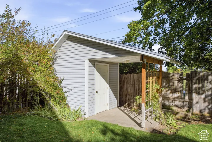 Detached storage shed featuring grey horizontal siding, a covered concrete patio, and an integrated wood lattice trellis
