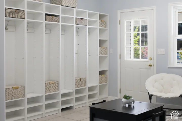 Custom white built-in cabinetry featuring floor-to-ceiling storage units with integrated shelving and wall-mounted hooks, complemented by a white exterior door with multi-pane glass inserts and light-toned tile flooring