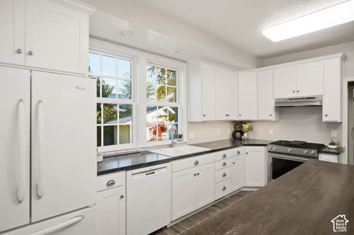 Kitchen featuring white cabinetry, dark countertops, a farmhouse-style sink, stainless steel gas range, and wood-finish flooring