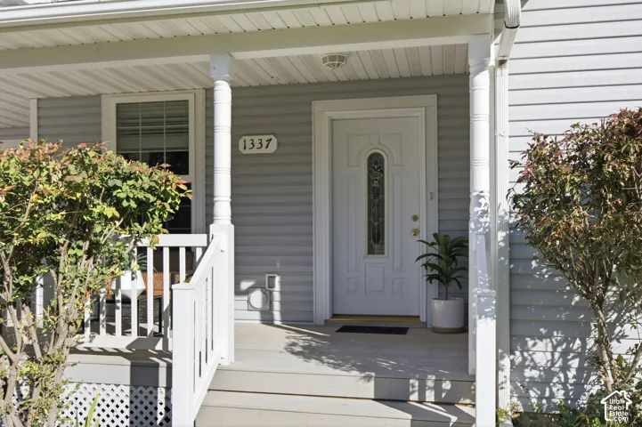 Covered front porch featuring white railings, spindle columns, light gray siding, and an entry door with an oval glass insert
