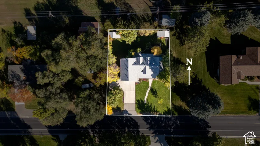 Aerial perspective of a property featuring a rectangular lot, mature perimeter landscaping, concrete driveway, stone-paved walkway, and two detached storage structures