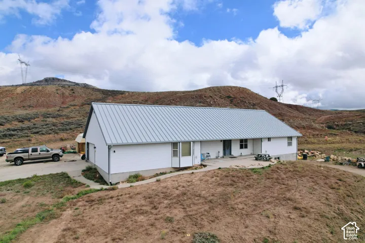 Single-story residence featuring a standing seam metal roof, white siding, concrete porch, and bay window, set against a mountainous landscape