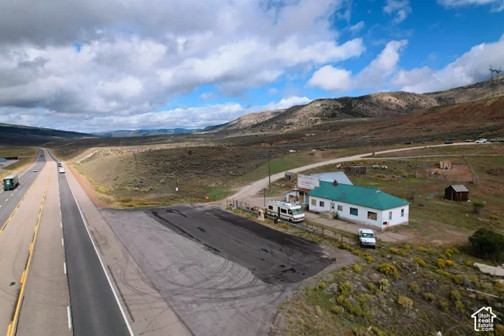 Single-story structure with a metal roof, expansive acreage, paved parking area, and mountain terrain backdrop